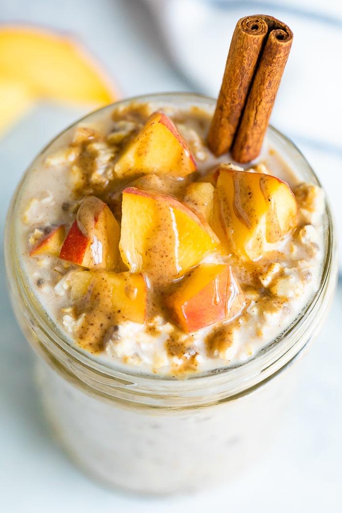 Overhead shot of peach overnight oats topped with peaches, almond butter and a cinnamon stick.