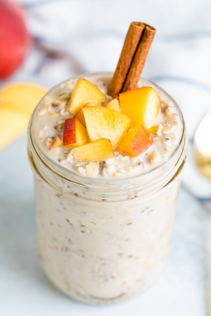 Peach overnight oats in a mason jar with fresh chopped peaches on top and a cinnamon stick.