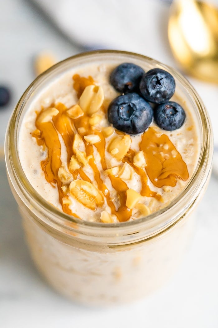 Overhead shot of peanut butter overnight oats in a mason jar topped with blueberries, chopped peanuts and a peanut butter drizzle.