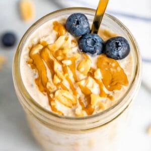 Overhead shot of peanut butter overnight oats in a mason jar topped with blueberries, chopped peanuts and a peanut butter drizzle.