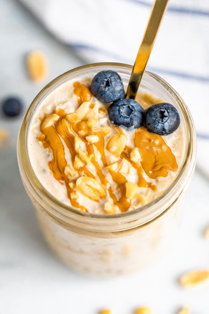 Overhead shot of peanut butter overnight oats in a mason jar topped with blueberries, chopped peanuts and a peanut butter drizzle.