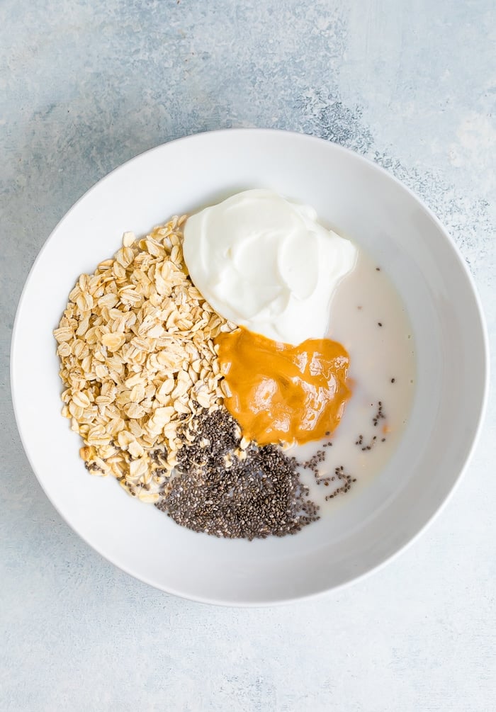 Ingredients for peanut butter overnight oats in a white bowl before mixing.