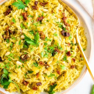 Bowl of pesto spaghetti squash salad topped with parsley and sun-dried tomatoes.