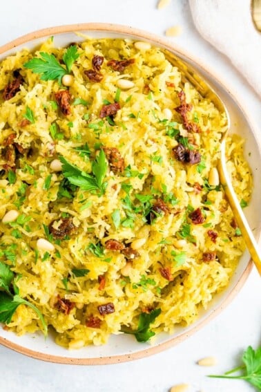 Bowl of pesto spaghetti squash salad topped with parsley and sun-dried tomatoes.