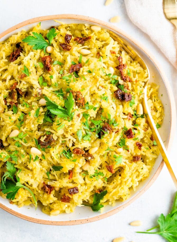 Bowl of pesto spaghetti squash salad topped with parsley and sun-dried tomatoes.