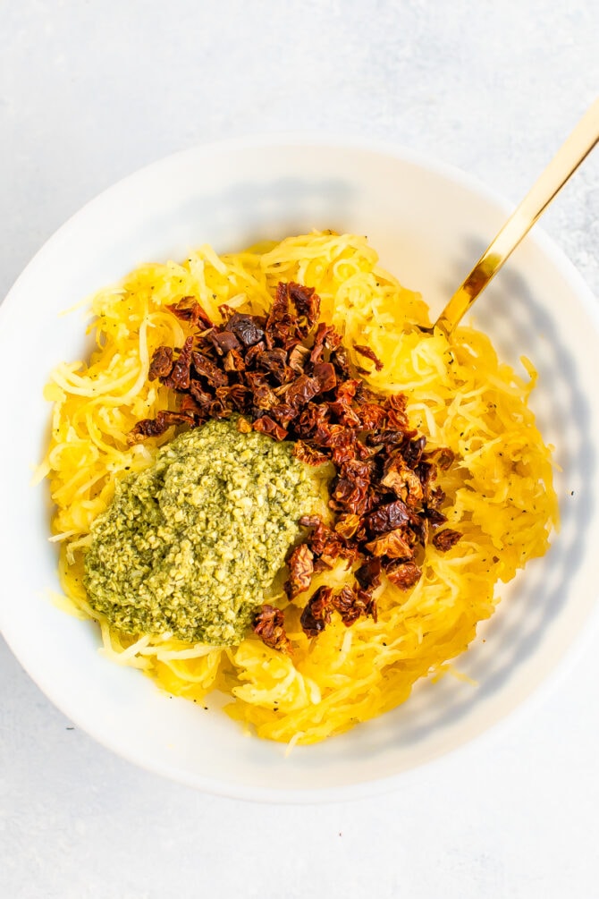 Mixing bowl with spaghetti squash, pesto and chopped sun-dried tomatoes before being mixed together.