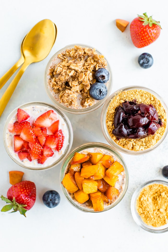 Overhead shot with four mason jars with different overnight oat flavors: cherry cheesecake, peach pie, strawberry and blueberry crumble