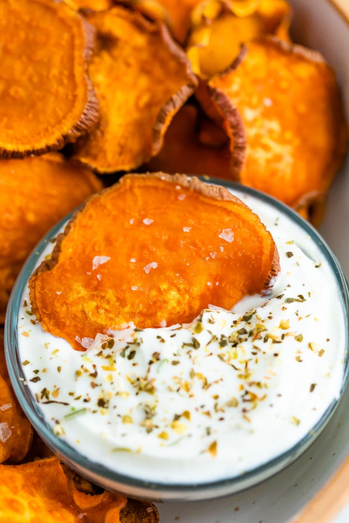 Sweet potato chips in a bowl and one chip being dipped into a bowl of creamy dip.