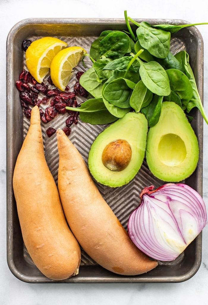 Lemon, cranberries, spinach, avocado, sweet potatoes and red onion on a sheet pan.