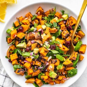 Bowl of roasted sweet potato salad with cranberries, onion, spinach and avocado.