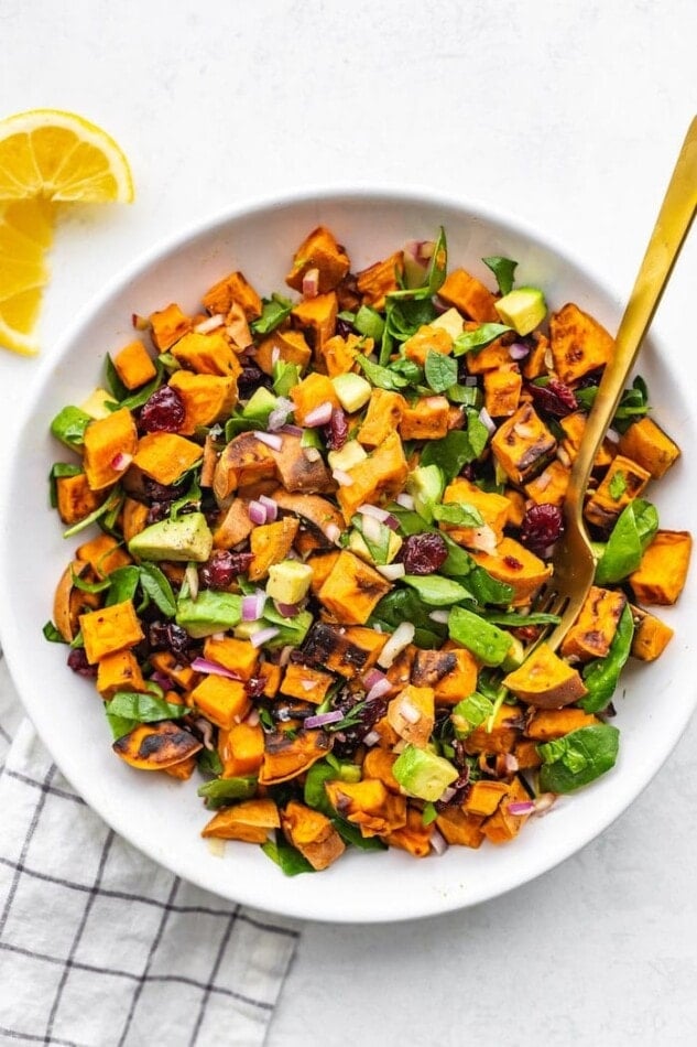 Bowl of roasted sweet potato salad with cranberries, onion, spinach and avocado.