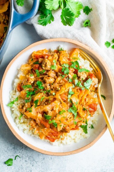 Overhead shot of unstuffed cabbage roll bowl. Cabbage and turkey are mixed with a tomato sauce are served over rice in a white ceramic bowl. Gold fork is resting inside the bowl.