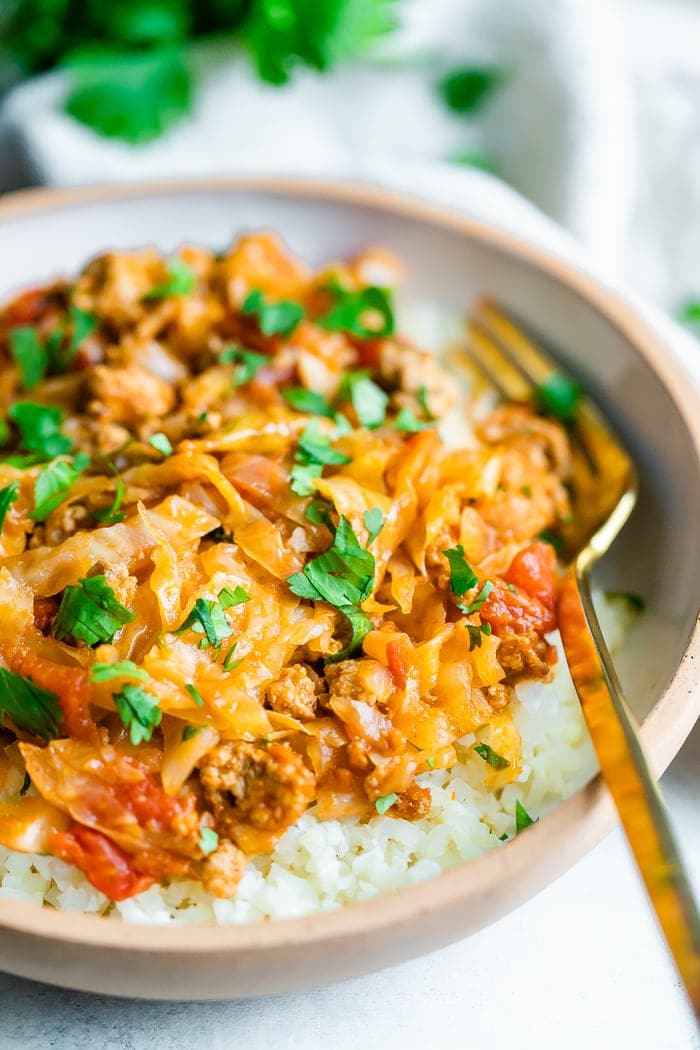 Close up shot of unstuffed cabbage roll bowl. Cabbage and turkey are mixed with a tomato sauce and served over rice. Gold fork is resting inside white ceramic bowl.