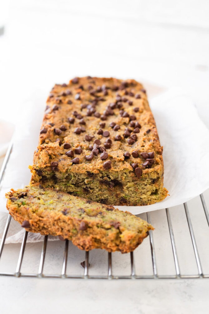 Loaf of chocolate chip zucchini bread on a cloth and cooking rack with one slice cut.