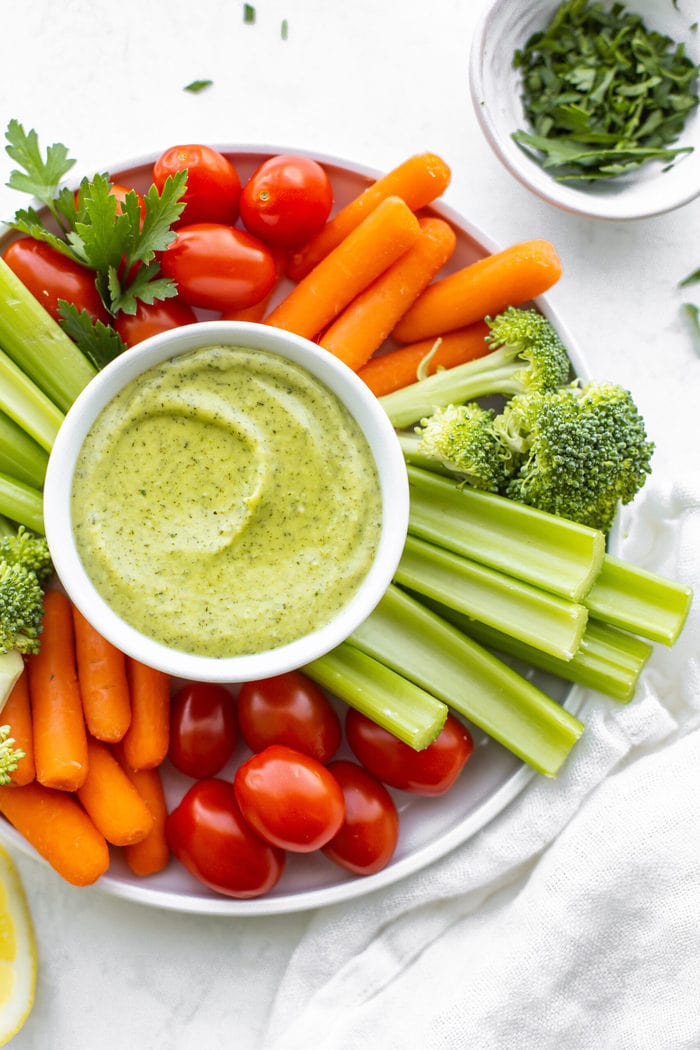 Veggie tray platter with tomatoes, carrots, celery, broccoli and avocado ranch dip in a white bowl.