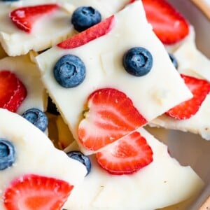 Square of frozen yogurt bark topped with berries and coconut in a bowl.
