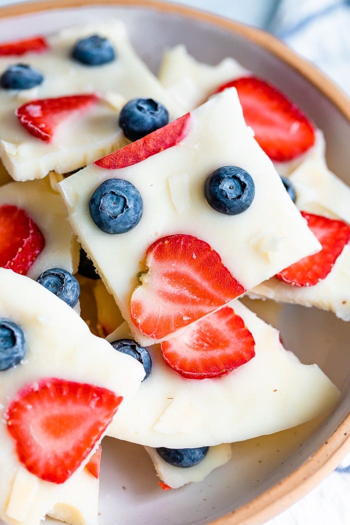 Square of frozen yogurt bark topped with berries and coconut in a bowl.