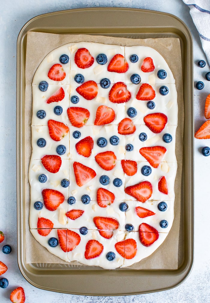 Frozen yogurt bark topped with berries and coconut flakes on a cookie sheet.