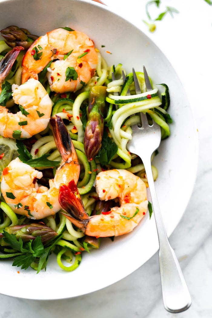 Bowl with zucchini noodles, asparagus and shrimp garnished with lemon and red pepper flakes.