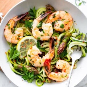 Bowl with zucchini noodles, asparagus and shrimp garnished with lemon and red pepper flakes.