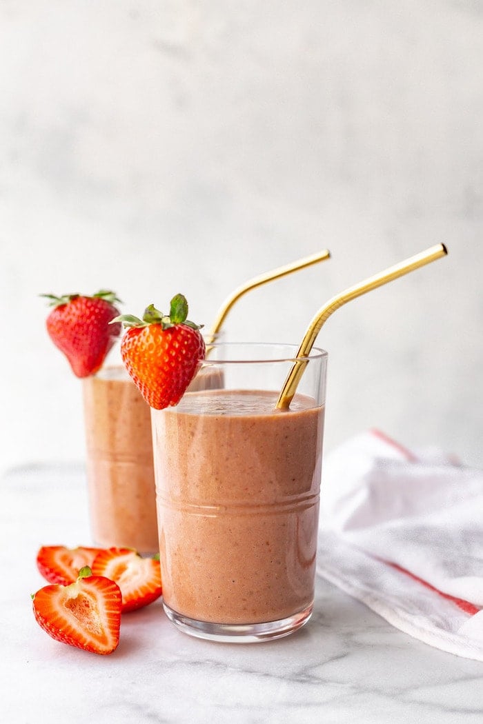 Two glasses full of chocolate strawberry smoothies. Metal straws are in the glass, and strawberries garnish the glass.