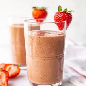 Two glasses with chocolate strawberry smoothies. Each glass has a strawberry on the rim.