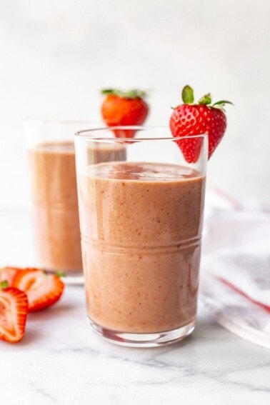 Two glasses with chocolate strawberry smoothies. Each glass has a strawberry on the rim.