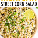 Bird's eye view photo of a bowl of Mexican Street Corn Salad topped with lime and fresh cilantro. Bowl is resting on a striped napkin.