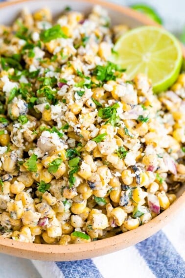 Close up photo of Mexican street corn salad in a bowl garnished with cilantro and lime. Corn is tossed in a light creamy dressing.