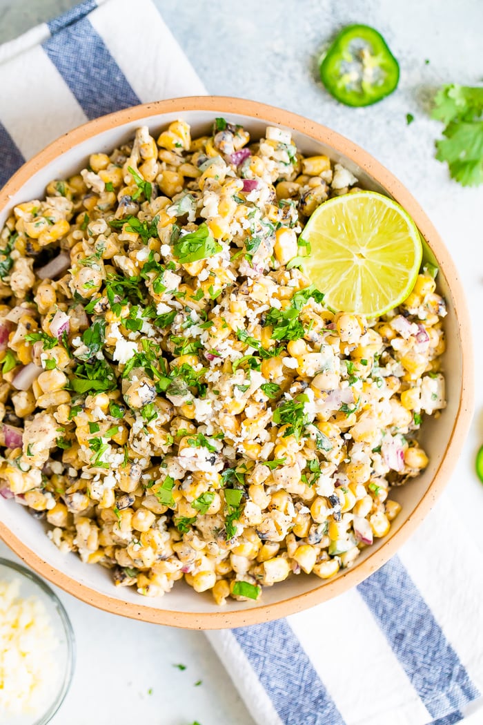 Bird's eye view photo of a bowl of Mexican Street Corn Salad topped with lime and fresh cilantro. Bowl is resting on a striped napkin.