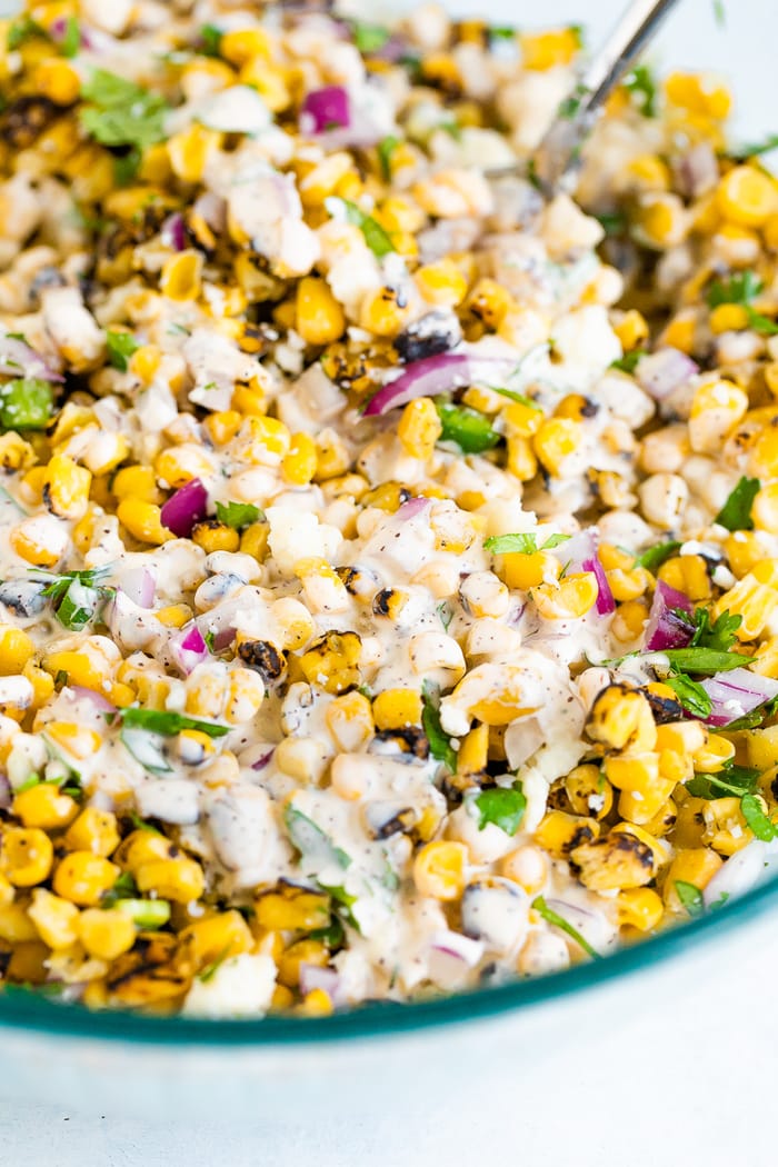 Close up photo of Mexican street corn salad in a bowl. Corn, red onion and cilantro drizzled with a creamy dressing.