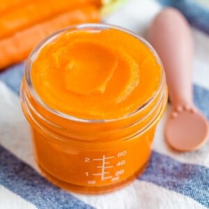 Glass baby food jar with carrot puree with an ezpz spoon dipped in.