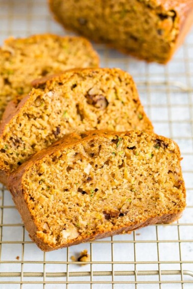 Close up photo of three thick slices of zucchini bread on a gold cooling rack.