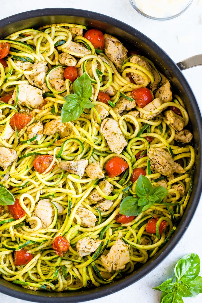 Skillet with pesto zucchini noodles with basil, chicken and tomatoes.