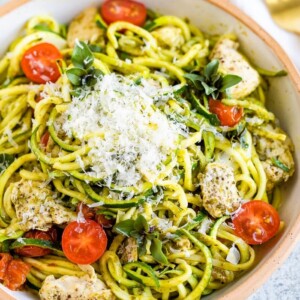 Ceramic bowl with pesto zucchini noodles with chicken and cherry tomatoes, topped with parmesan.