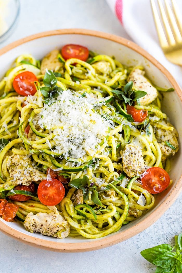 Ceramic bowl with pesto zucchini noodles with chicken and cherry tomatoes, topped with parmesan.