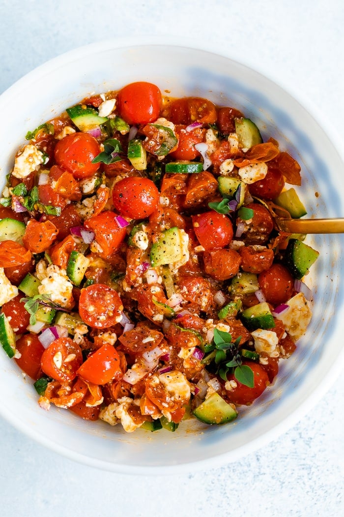 Mixing bowl with a tomato salad made with cucumbers, roasted tomatoes, onion, basil and feta.