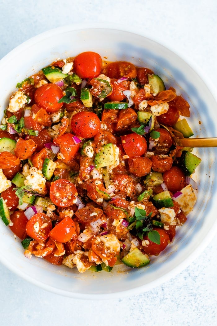 Mixing bowl with a tomato salad made with cucumbers, roasted tomatoes, onion, basil and feta.