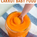 Glass baby food jar with carrot puree with an ezpz spoon dipped in.