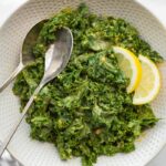 White bowl with garlicky kale salad and who silver serving spoons.