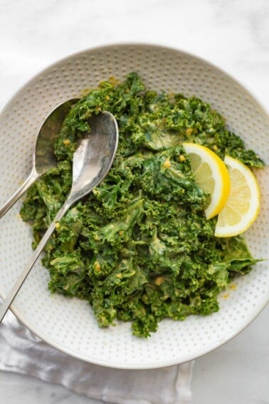 White bowl with garlicky kale salad and who silver serving spoons.