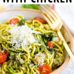 Bowl with pesto zucchini noodles with parmesan, chicken and tomatoes. Gold fork is resting on the side of the bowl.