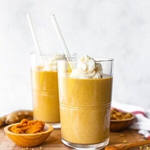 Two pumpkin gingerbread smoothies on a wood board topped with whipped cream.