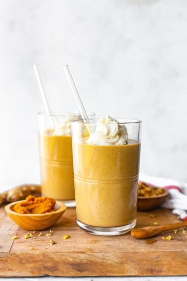 Two pumpkin gingerbread smoothies on a wood board topped with whipped cream.