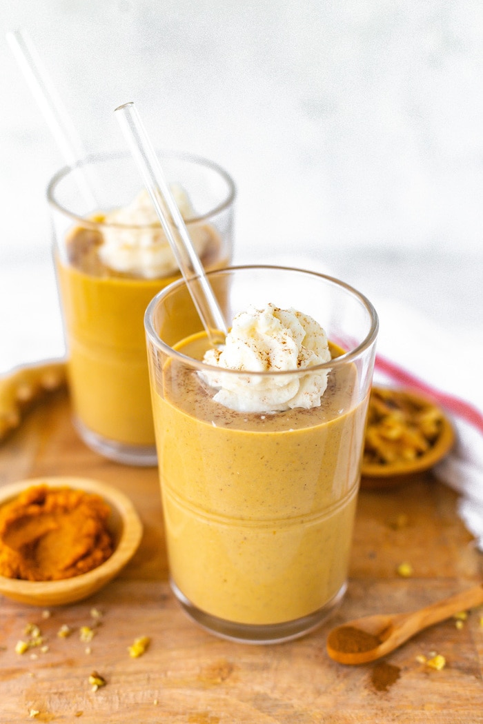 Two glasses of pumpkin gingerbread smoothies topped with whipped cream and a sprinkle of cinnamon.