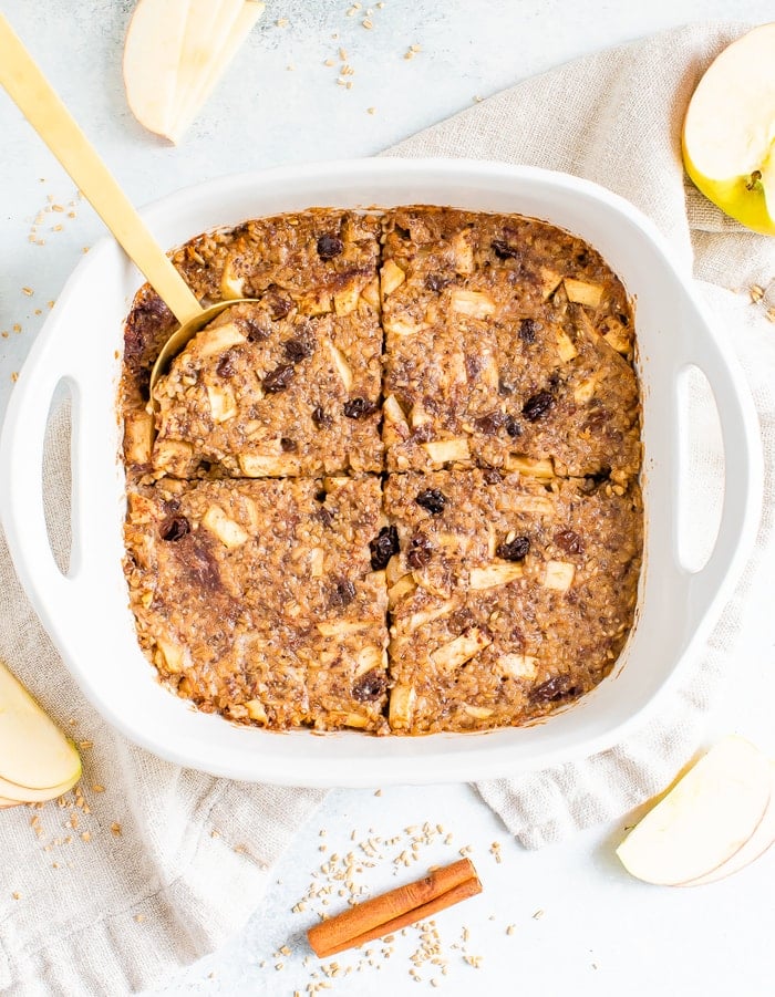 Apple cinnamon baked steel cut oatmeal in white baking dish with a gold spoon.