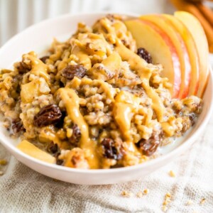 Baked apple steel cut oatmeal in a pink bowl with peanut butter drizzled on top.