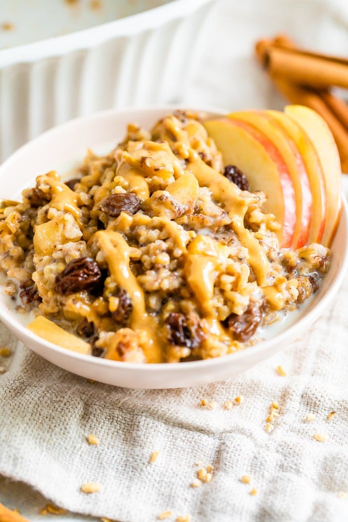 Baked apple steel cut oatmeal in a pink bowl with peanut butter drizzled on top.