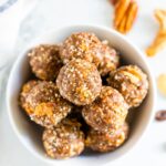 Bowl of apple pie energy balls. Pecans are on the table.