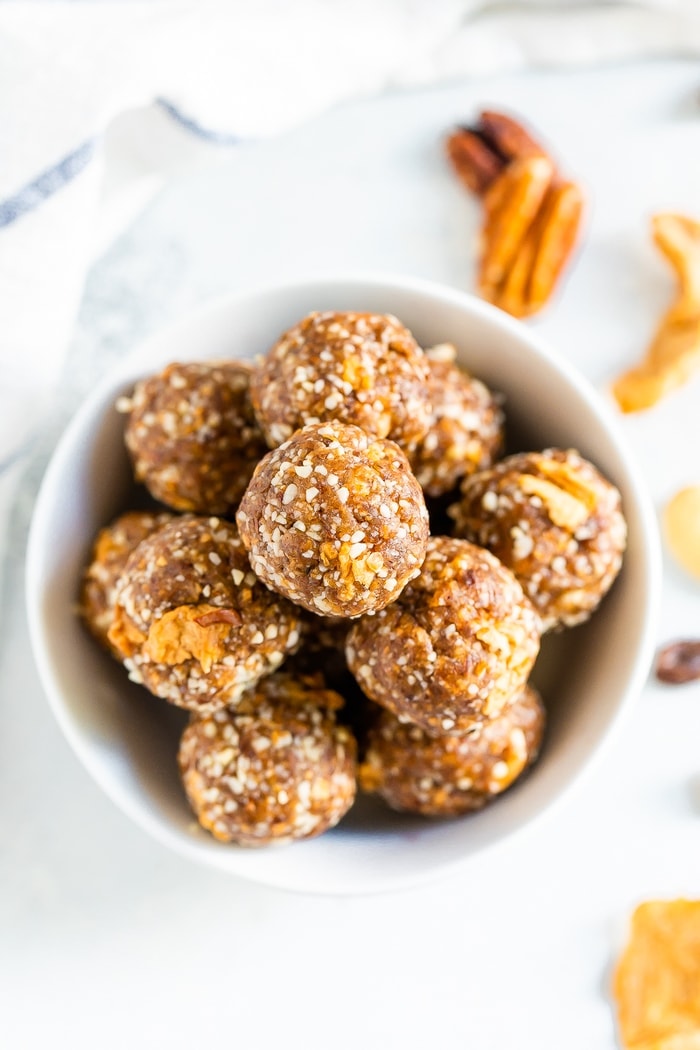 Bowl of apple pie energy balls. Pecans are on the table.